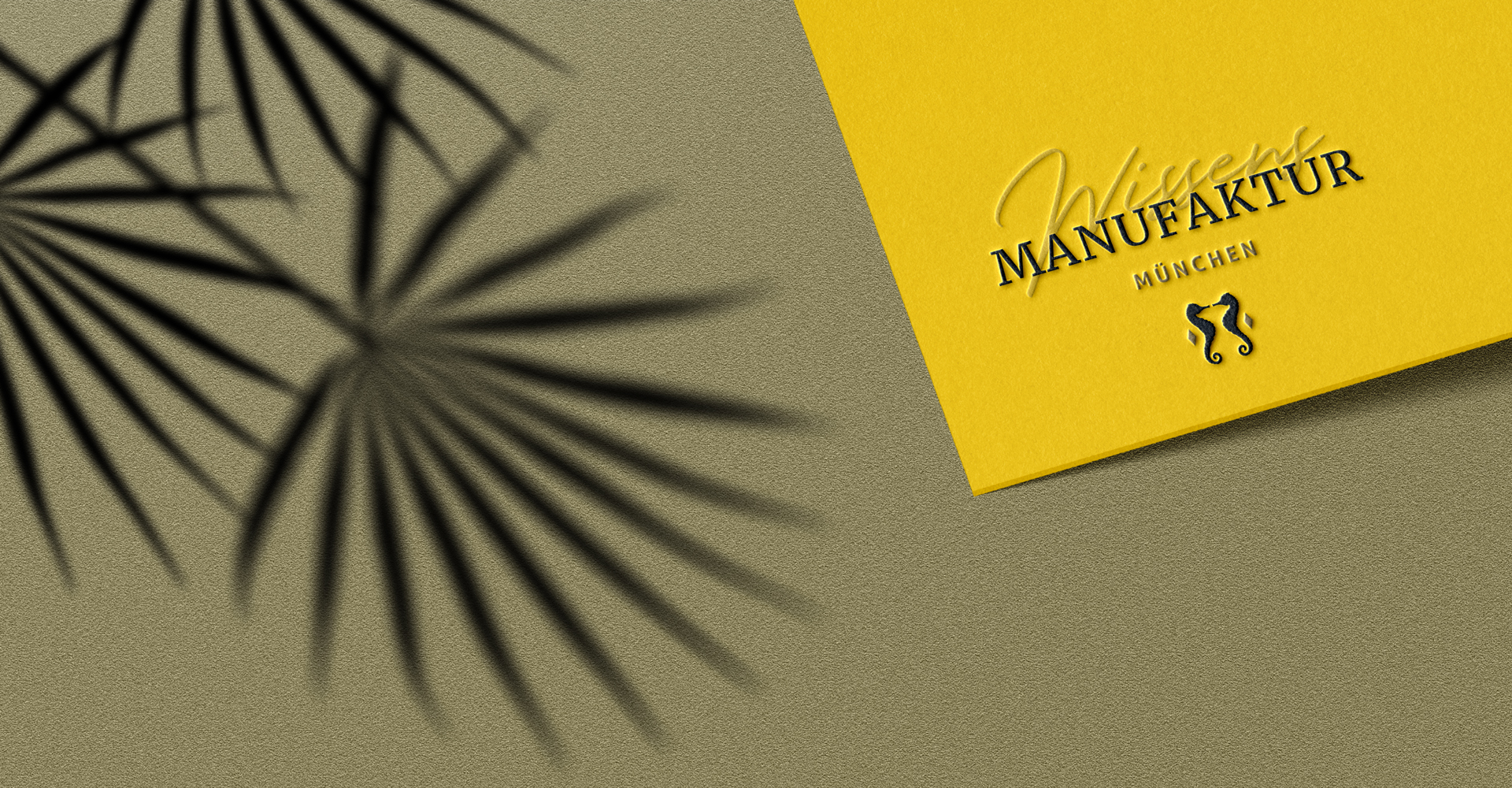 Banner der WissensMANUFAKTUR München mit geprägtem Branding auf gelbem Papier vor goldener Papierstruktur im Farbton #877F58 mit Palmenschatten